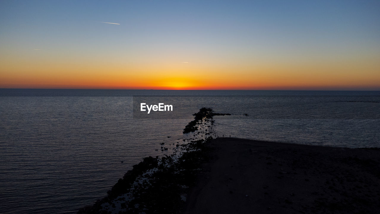 sea, water, sky, horizon, sunset, horizon over water, ocean, beauty in nature, scenics - nature, coast, dawn, beach, shore, nature, silhouette, wave, tranquility, land, tranquil scene, body of water, evening, one person, orange color, sun, idyllic, clear sky, outdoors, non-urban scene, sunlight, leisure activity, motion