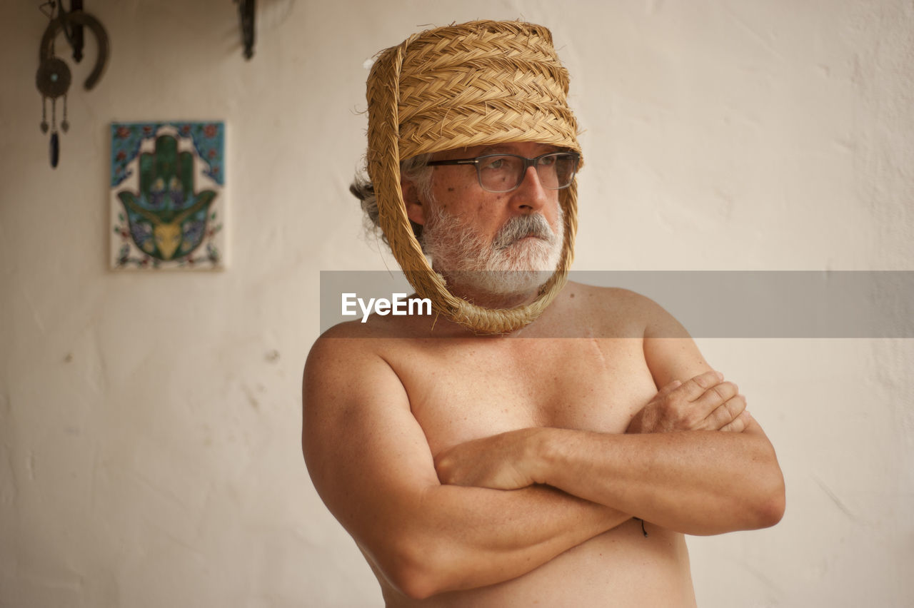 Shirtless senior man wearing wicker basket at home