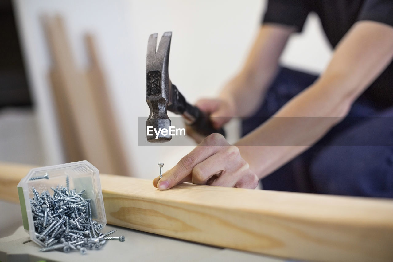 Midsection of female carpenter hammering nail into wooden plank