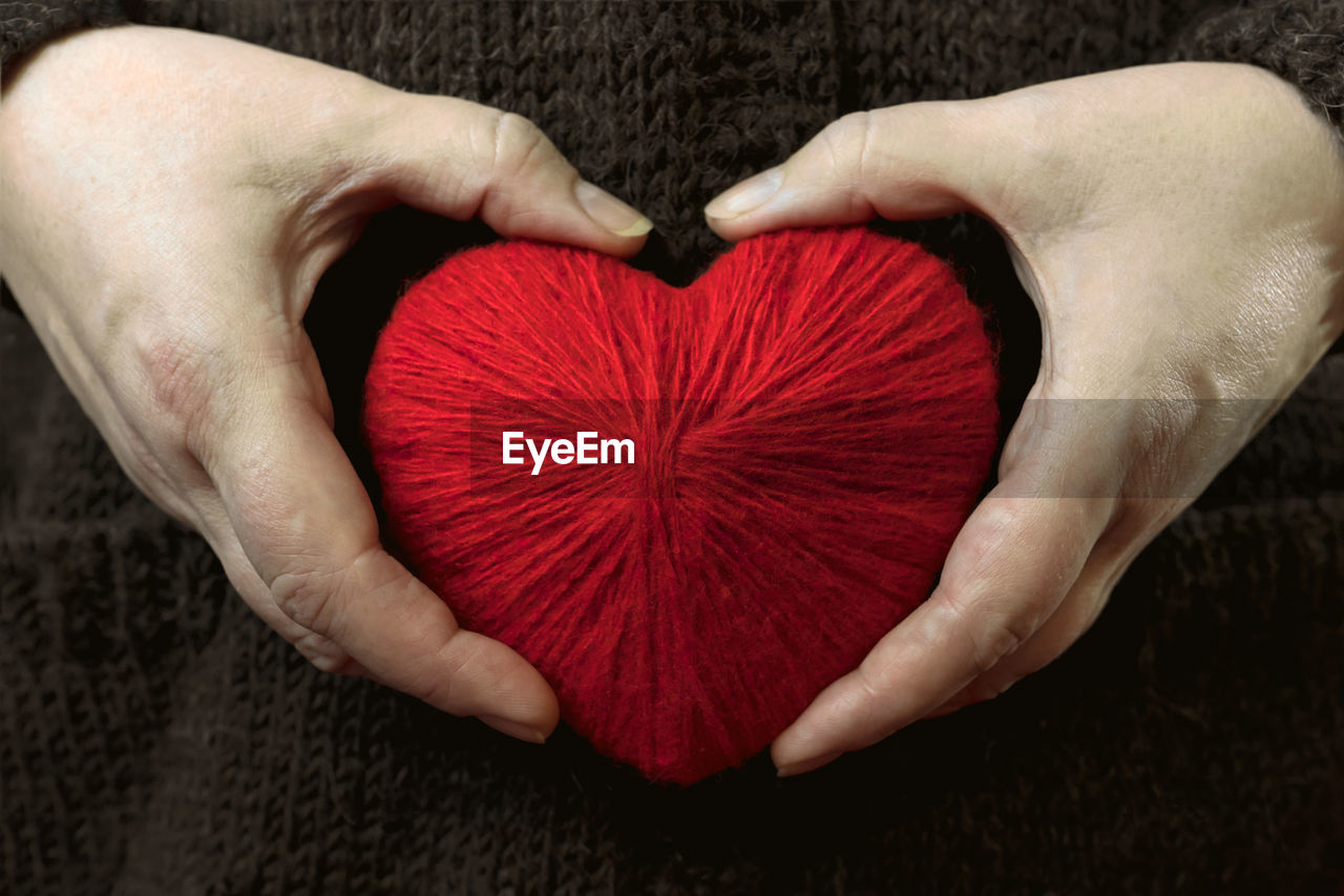 Close-up of hand holding red heart shape woolen yarn