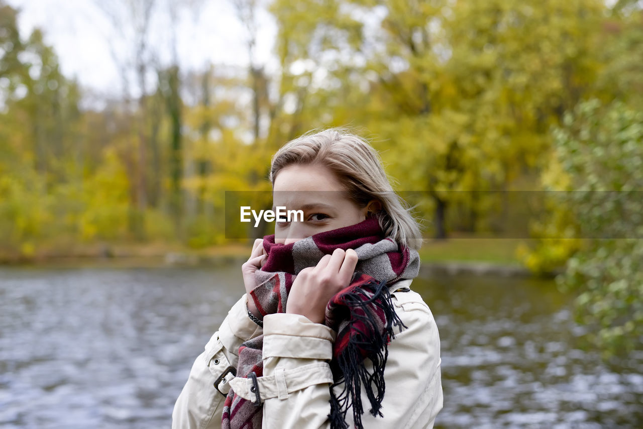 Portrait of young woman with covering face with scarf standing against lake