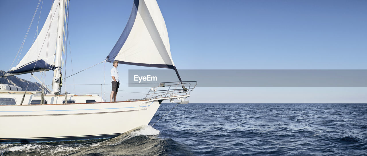 Mature man standing on his sailing boat looking at distance