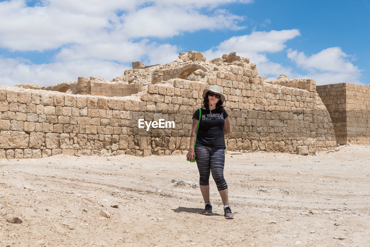 PORTRAIT OF YOUNG WOMAN STANDING AGAINST STONE WALL