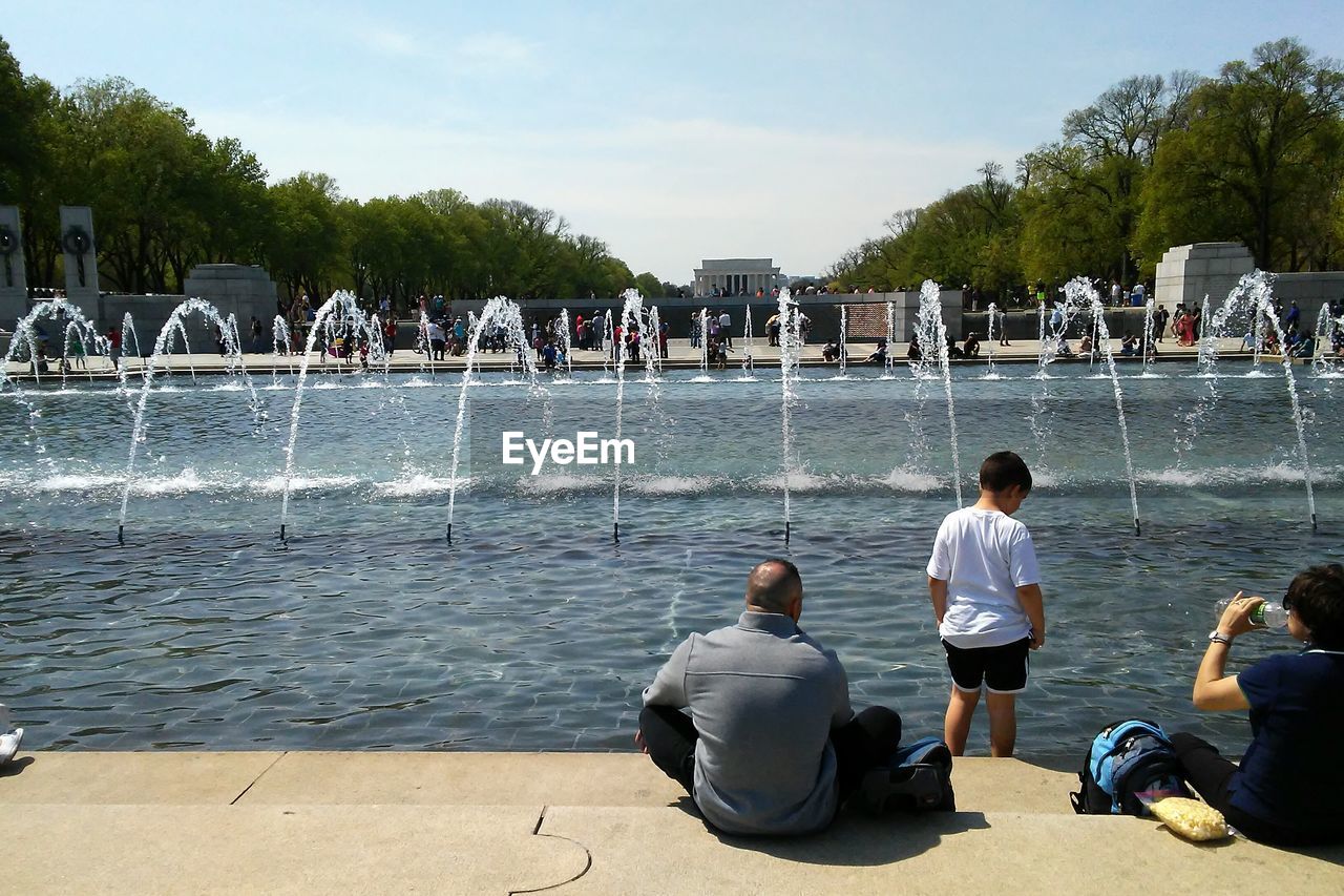 Rear view of people at fountain against sky