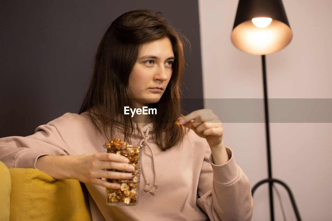 PORTRAIT OF YOUNG WOMAN HOLDING ILLUMINATED LAMP IN KITCHEN