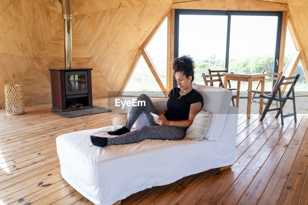 Woman using e reader while relaxing in a wooden dome tent.