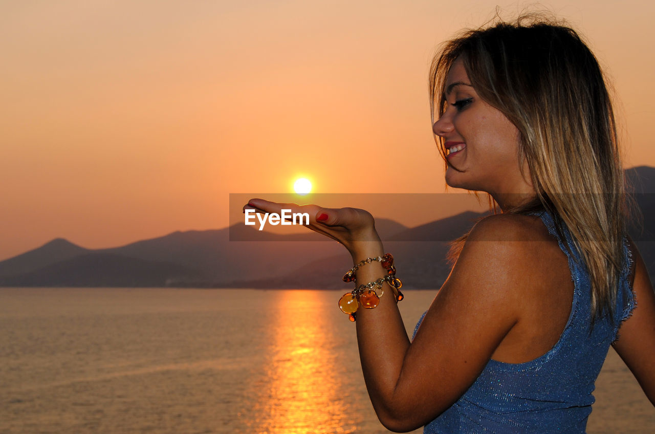 Side view of woman standing against sea during sunset