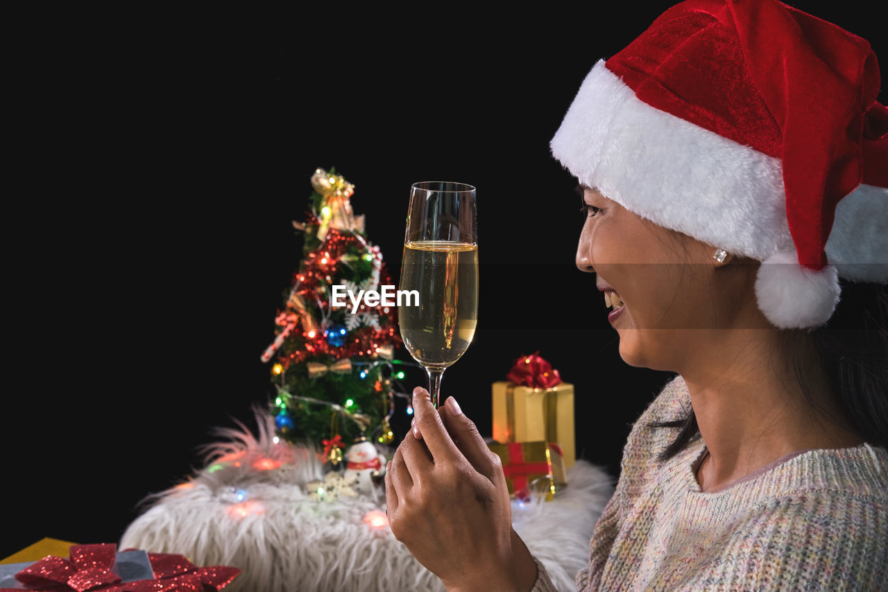 Smiling woman holding champagne flute against black background during christmas