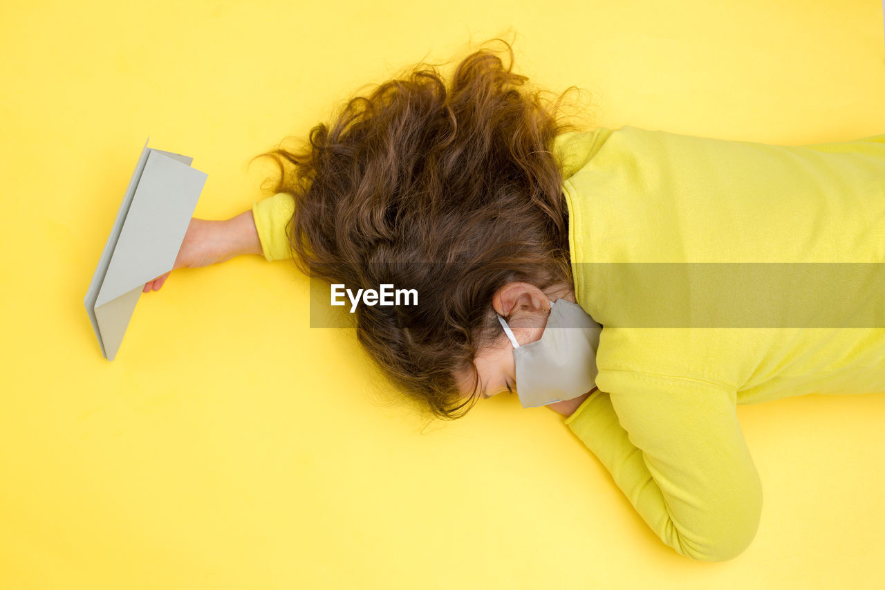 High angle view of girl lying down on yellow background