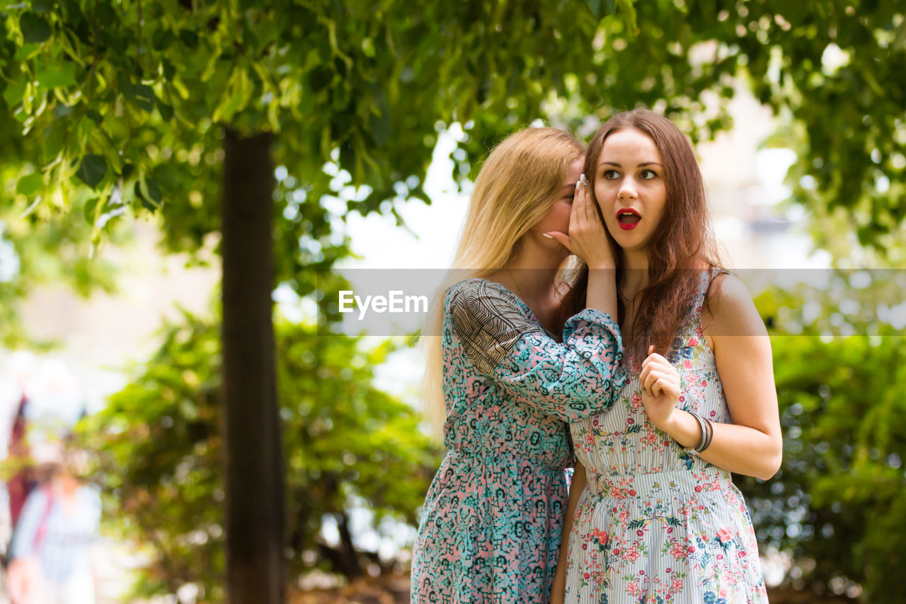 Woman whispering into friend ear while standing outdoors