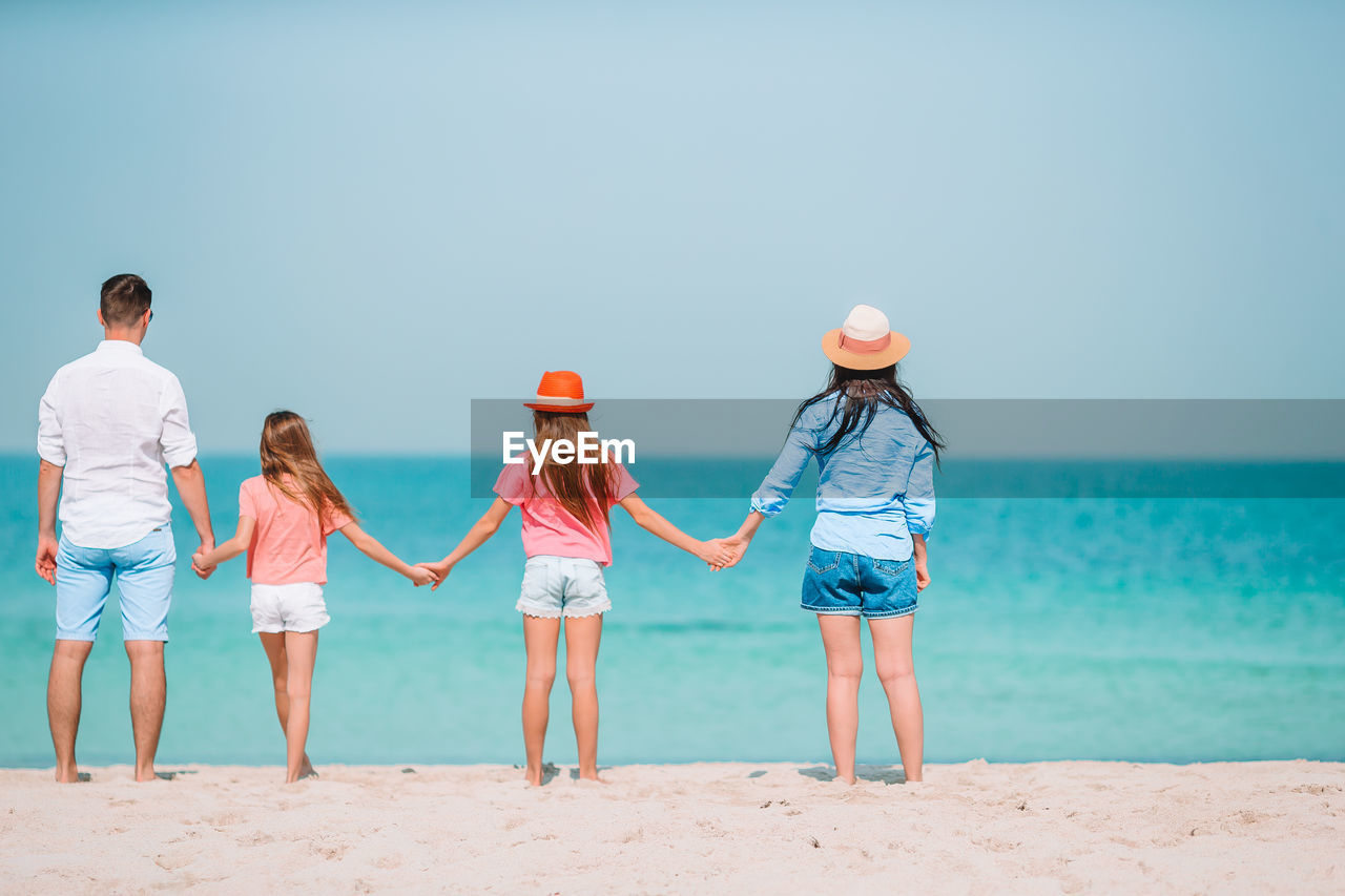 REAR VIEW OF WOMEN STANDING ON BEACH AGAINST SEA