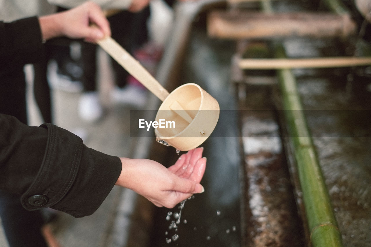 Cropped image of woman washing hand while pouring water from wooden spoon