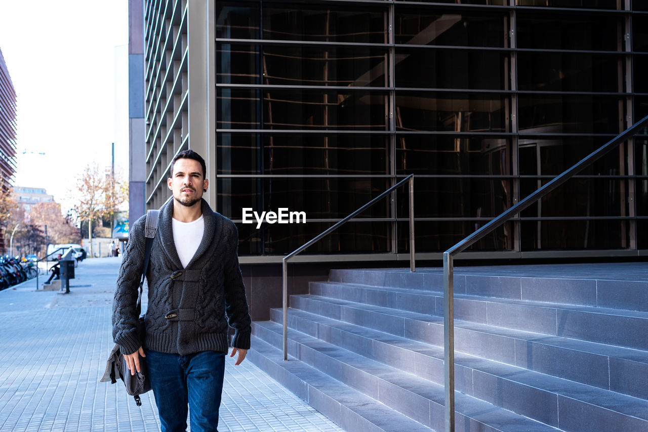 Young bearded man walking on the street next to office building