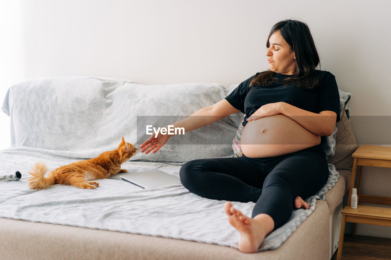 Pregnant middle-aged woman petting a cat while sitting on the couch. disabled cat.