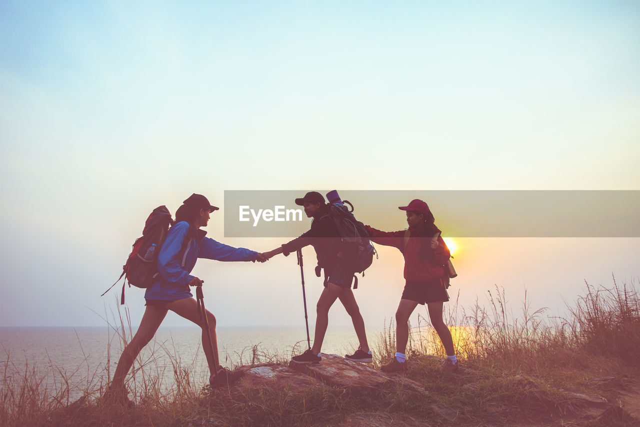 PEOPLE STANDING ON LAND DURING SUNSET