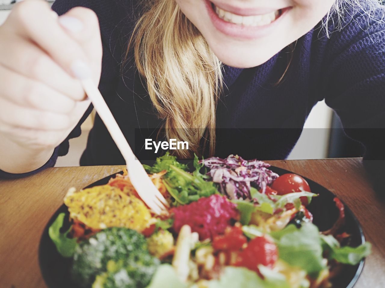 Midsection of happy woman eating salad at table