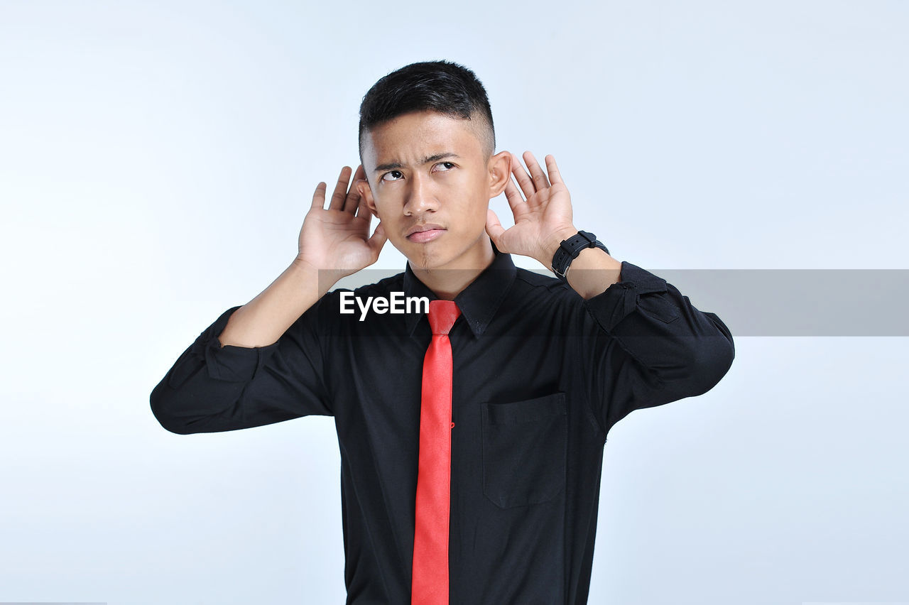 Young asian businessman listening with sign hand close to the ear.