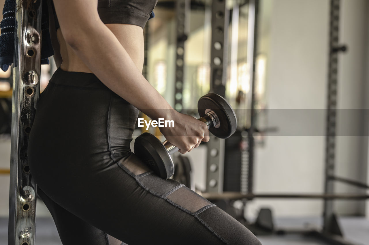 Midsection of woman lifting dumbbell in gym