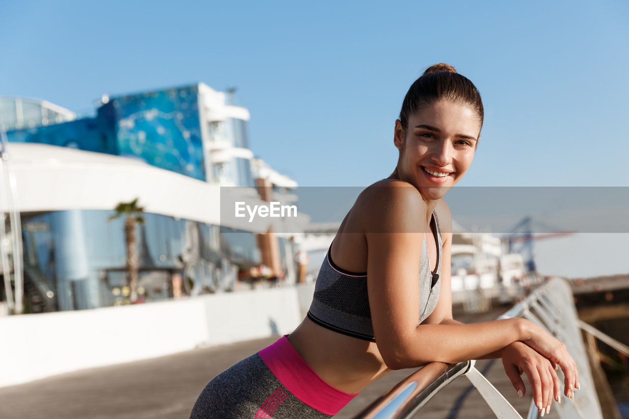 Portrait of smiling young woman standing by railing