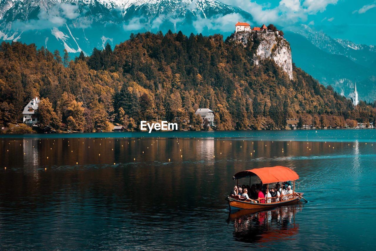 PEOPLE IN BOAT ON LAKE AGAINST MOUNTAIN