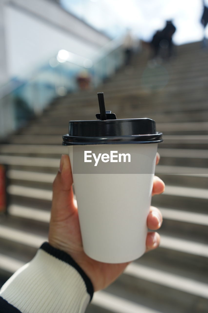 CLOSE-UP OF HAND HOLDING COFFEE CUP AND SPOON