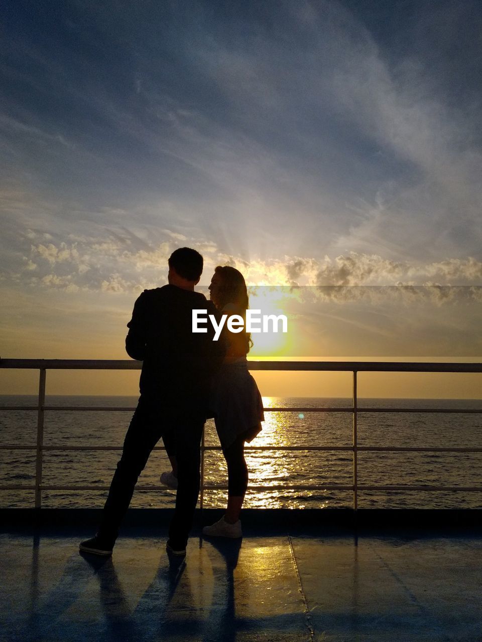 Couple standing on boat deck against sky during sunset