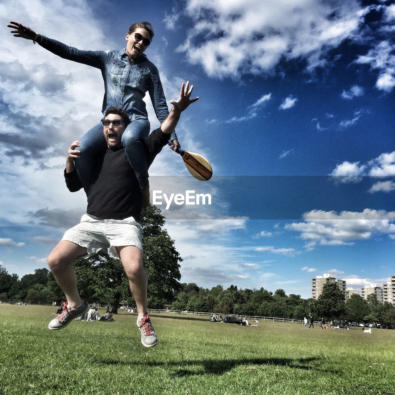 Cheerful man carrying girlfriend on shoulders while jumping at richmond park