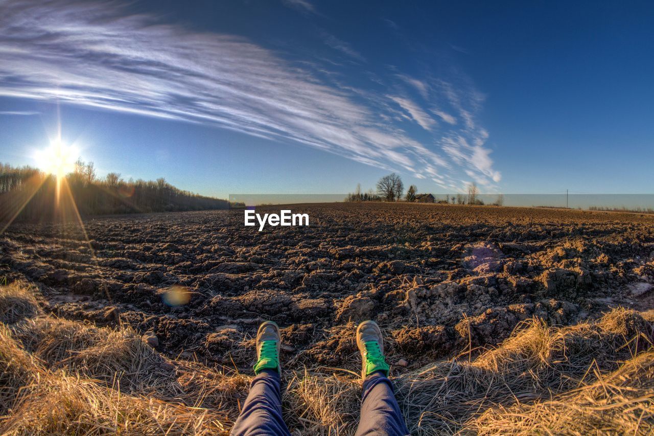 Low section of man resting on field against sky