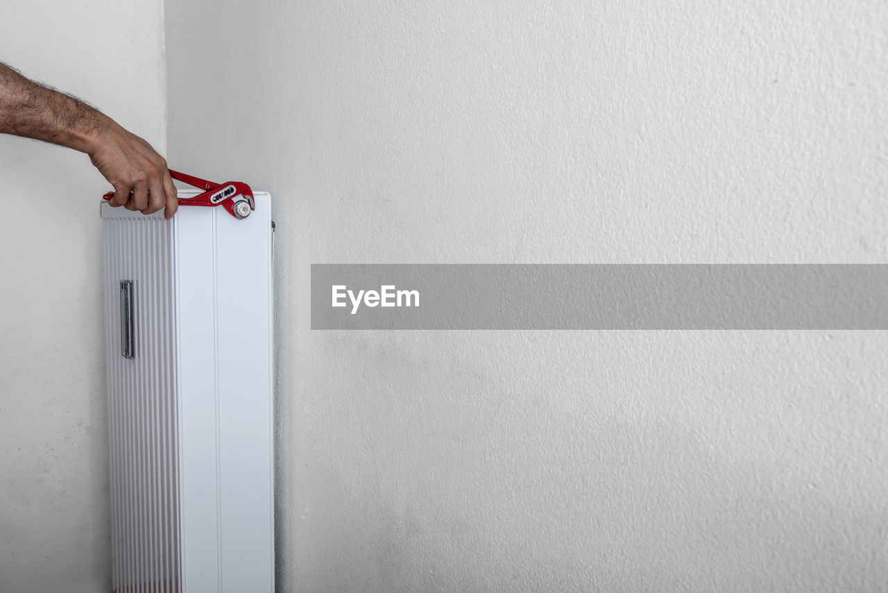 Close-up of mans hand repairing air conditioner against white wall at home