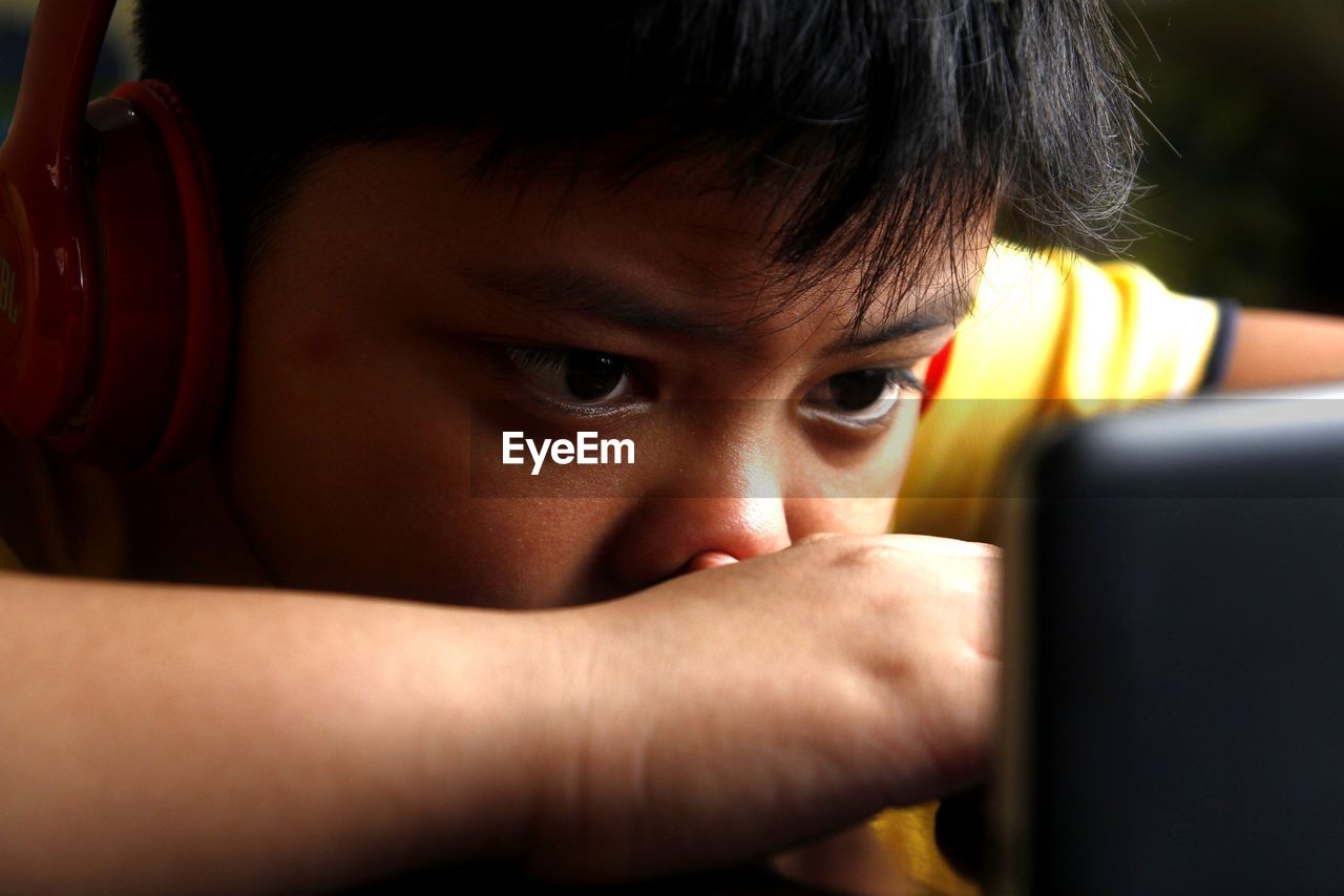 Close-up of boy listening to headphones while using smart phone