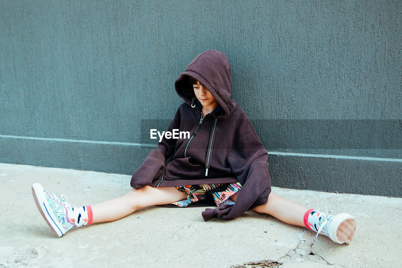 Street kid with big hooded jacket sitting against wall