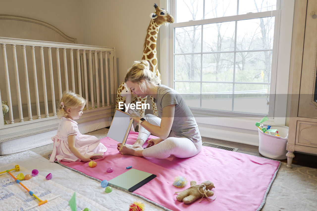 Young mom reading to her toddler daughter in her room