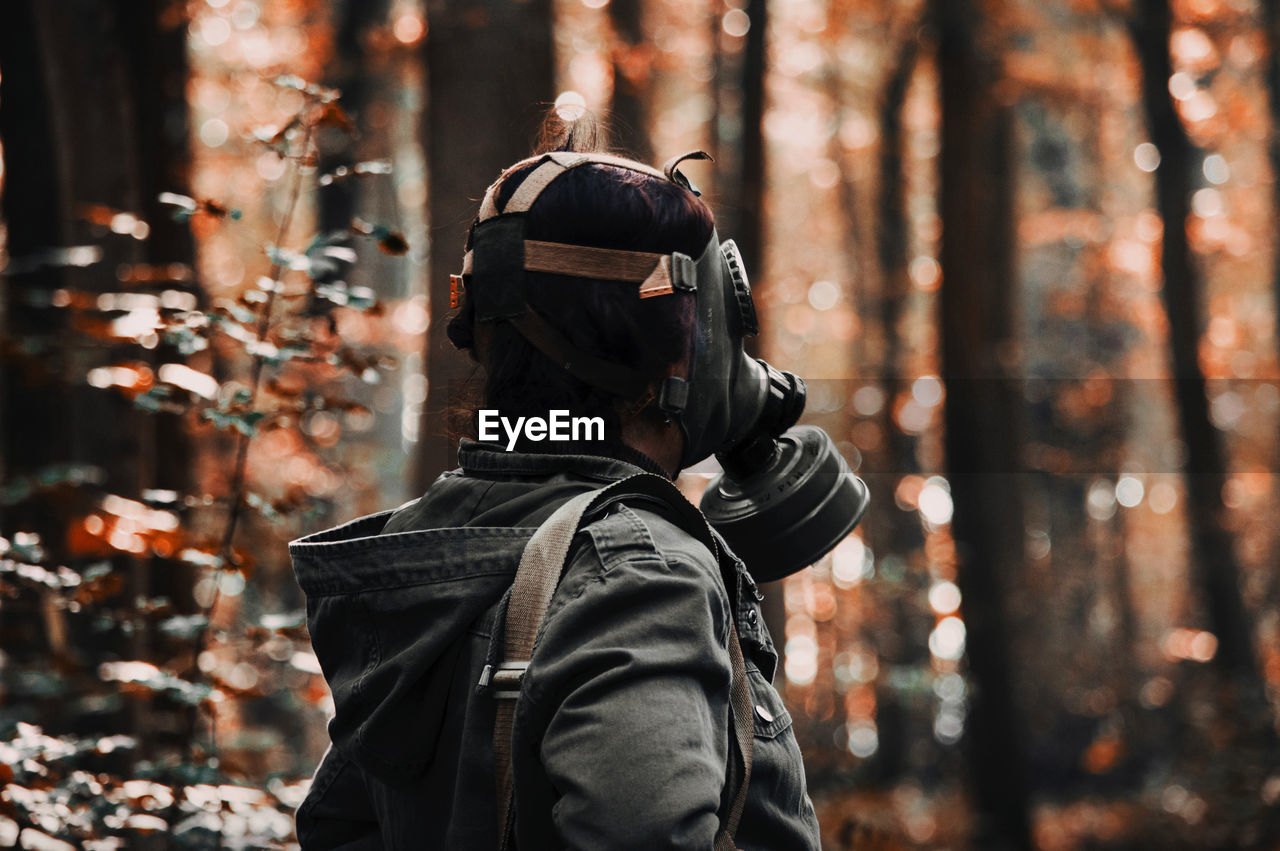 REAR VIEW OF MAN HOLDING CAMERA AT FOREST