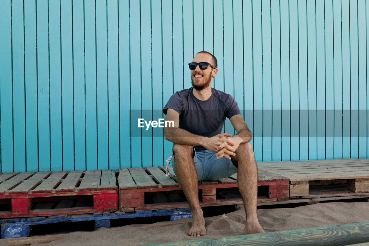 Smiling young man sitting against blue wall