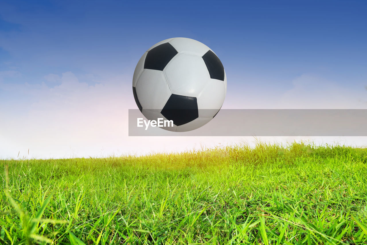 Digital composite image of soccer ball over field against blue sky