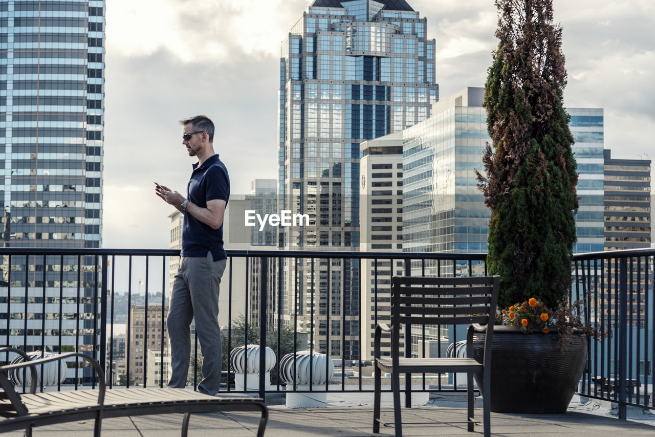 Side view of businessman using smart phone while standing on building terrace