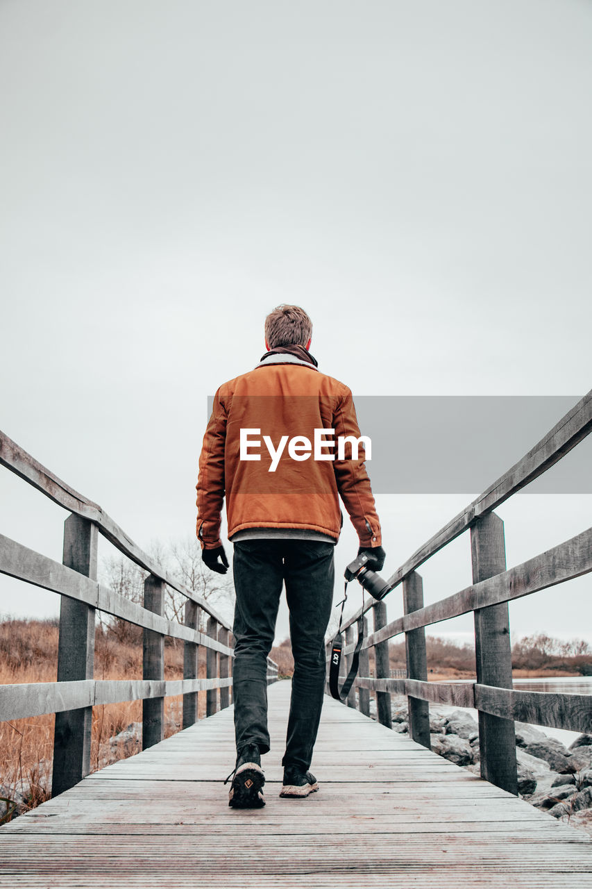 REAR VIEW OF MAN STANDING ON BRIDGE