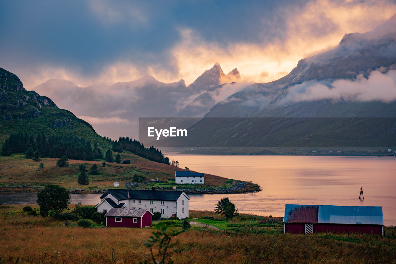 Houses by lake against mountains during sunset