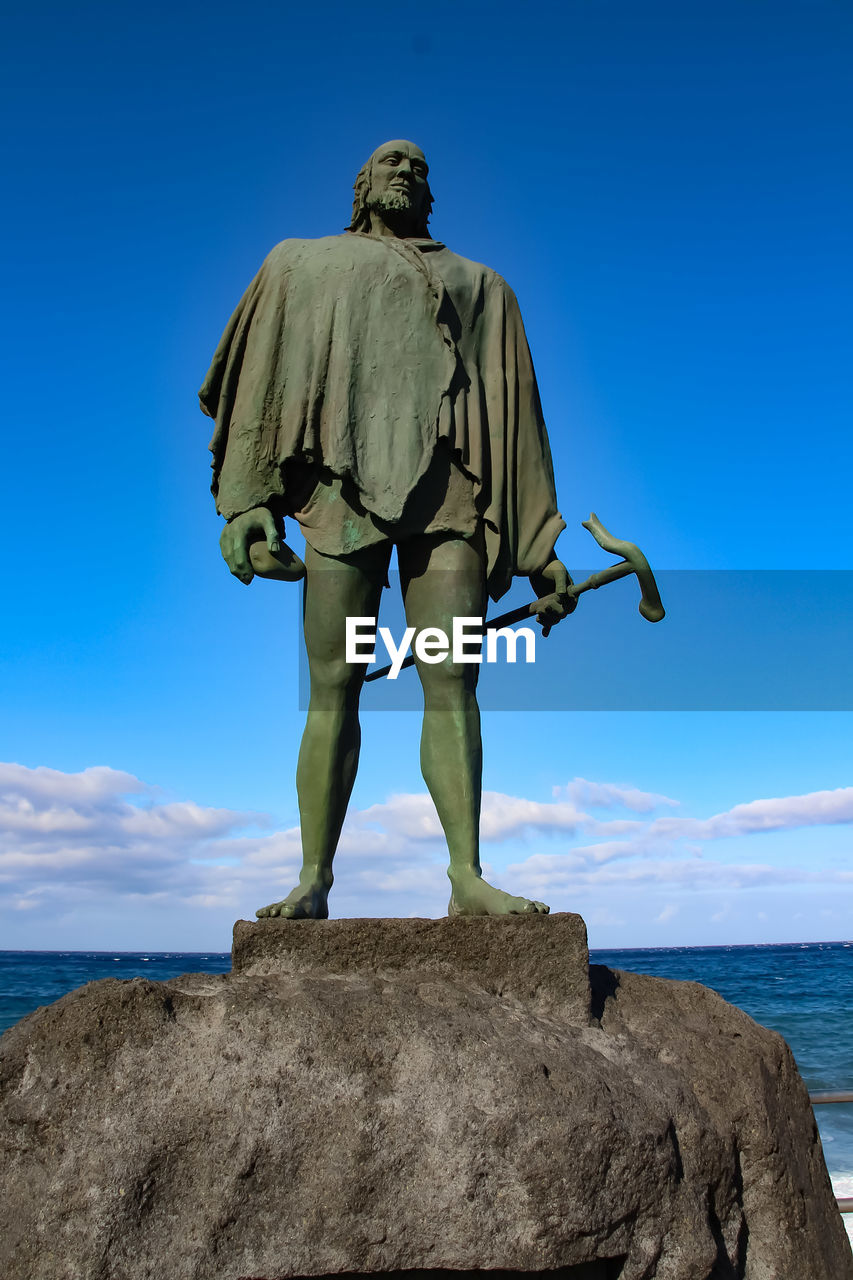 REAR VIEW OF MAN STANDING ON ROCK AGAINST SEA