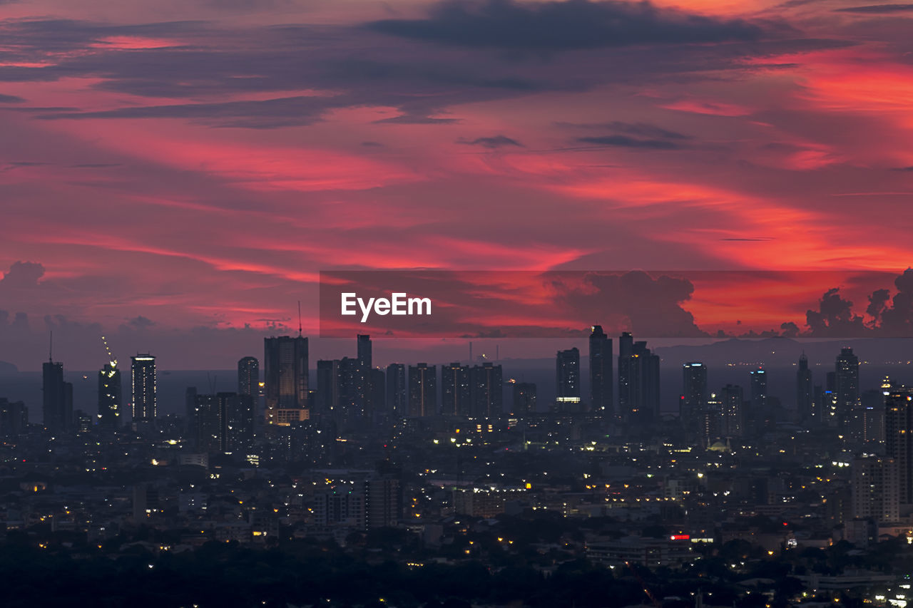 Illuminated buildings in city against crimson sky during sunset