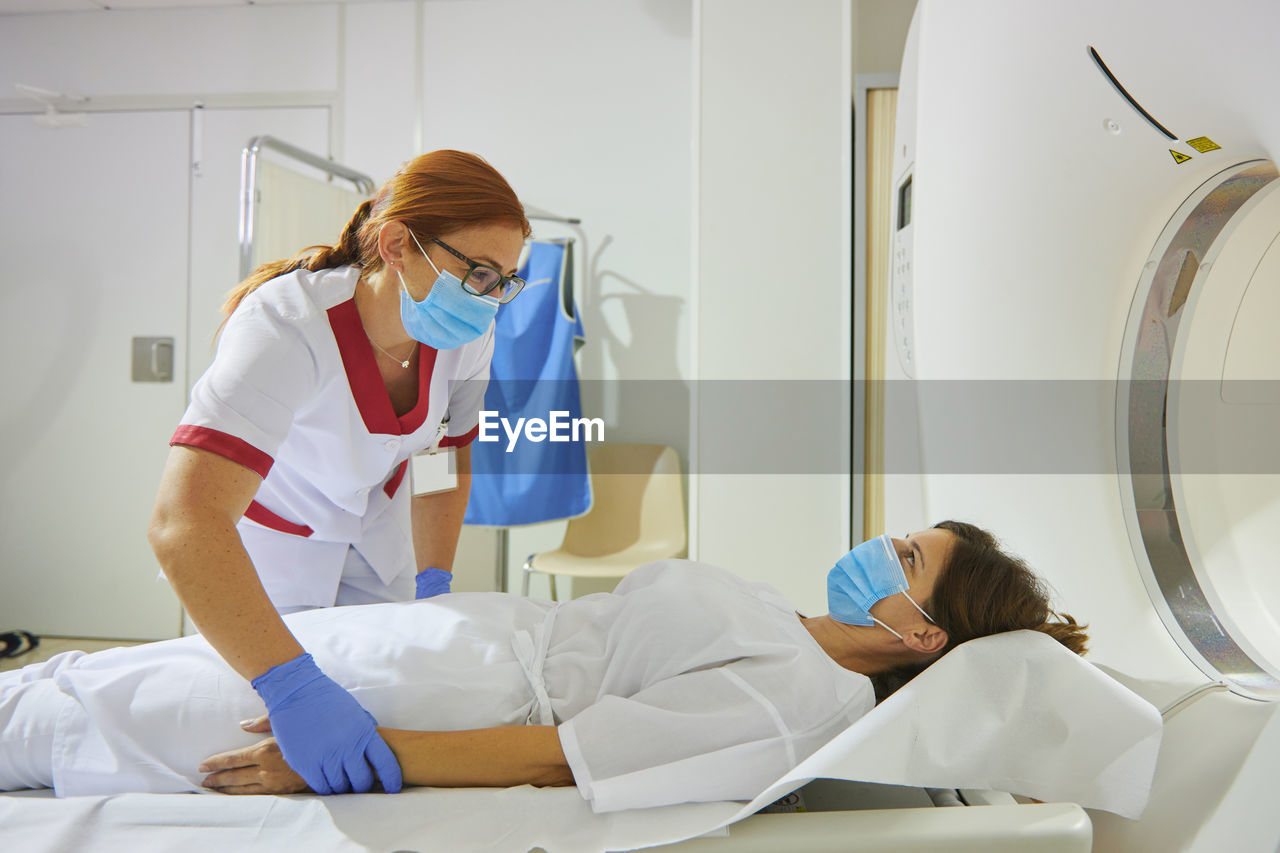 Doctor in uniform and eyeglasses using tomography machine with lying female patient in hospital