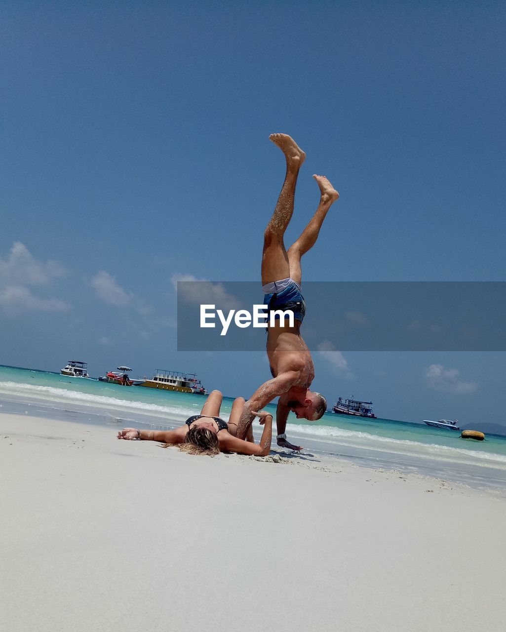 Full length of shirtless man doing handstand by woman at beach during summer