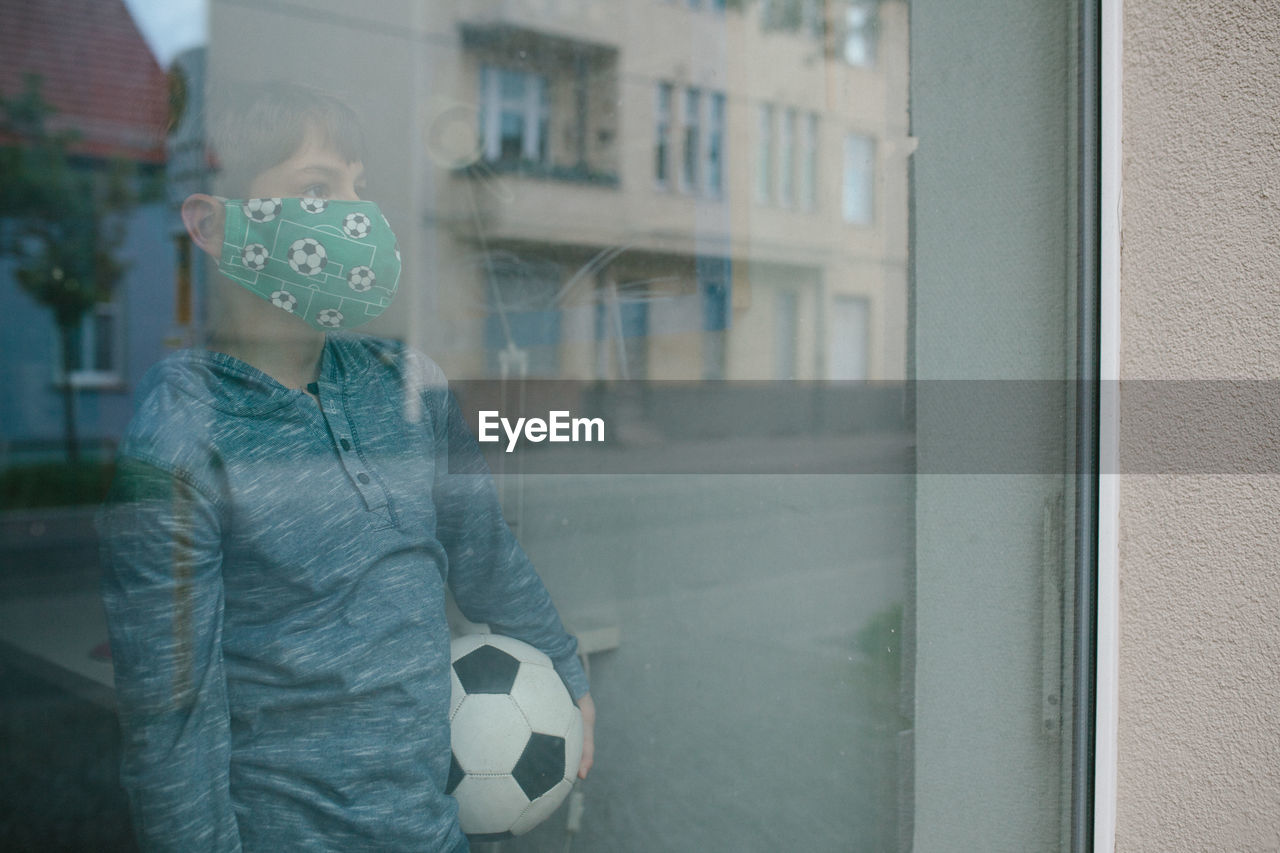 Boy with soccer ball standing by window