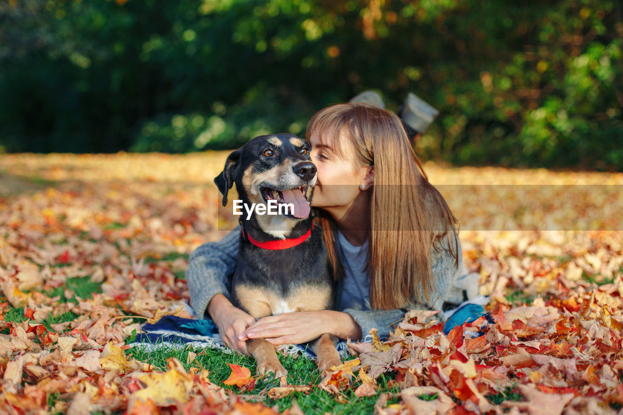 Young woman with dog lying on leaves during autumn