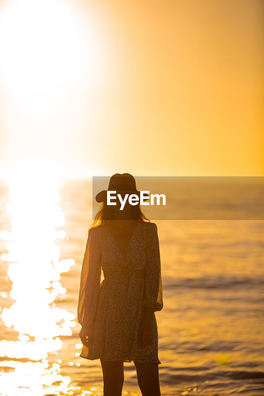 rear view of woman standing at beach against sky during sunset