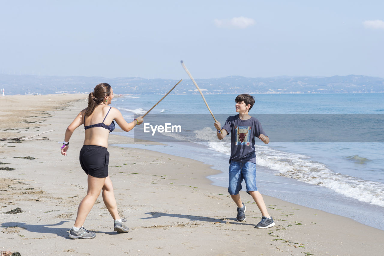 Two young friends playing with wooden swords on seashore