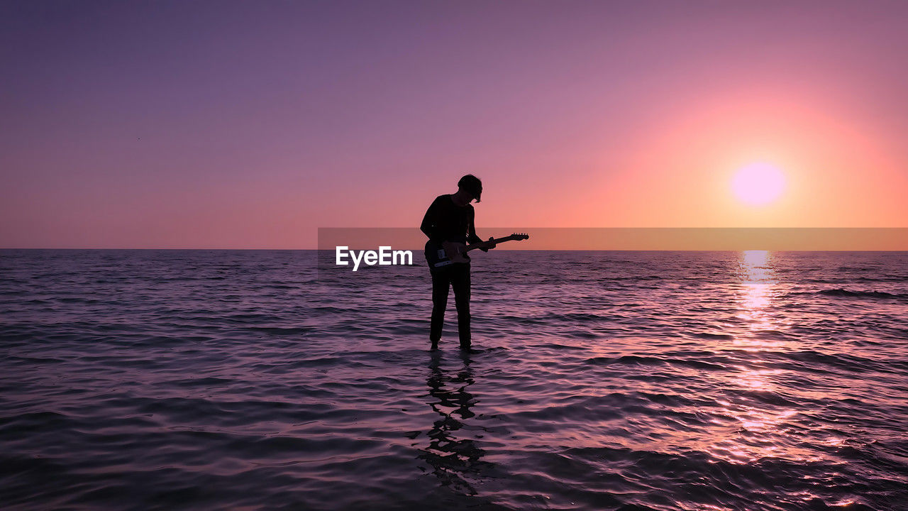 rear view of silhouette man standing at sea against sky during sunset