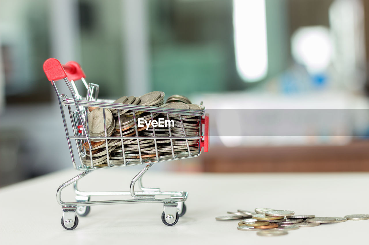 Close-up of miniature shopping cart with coins on table