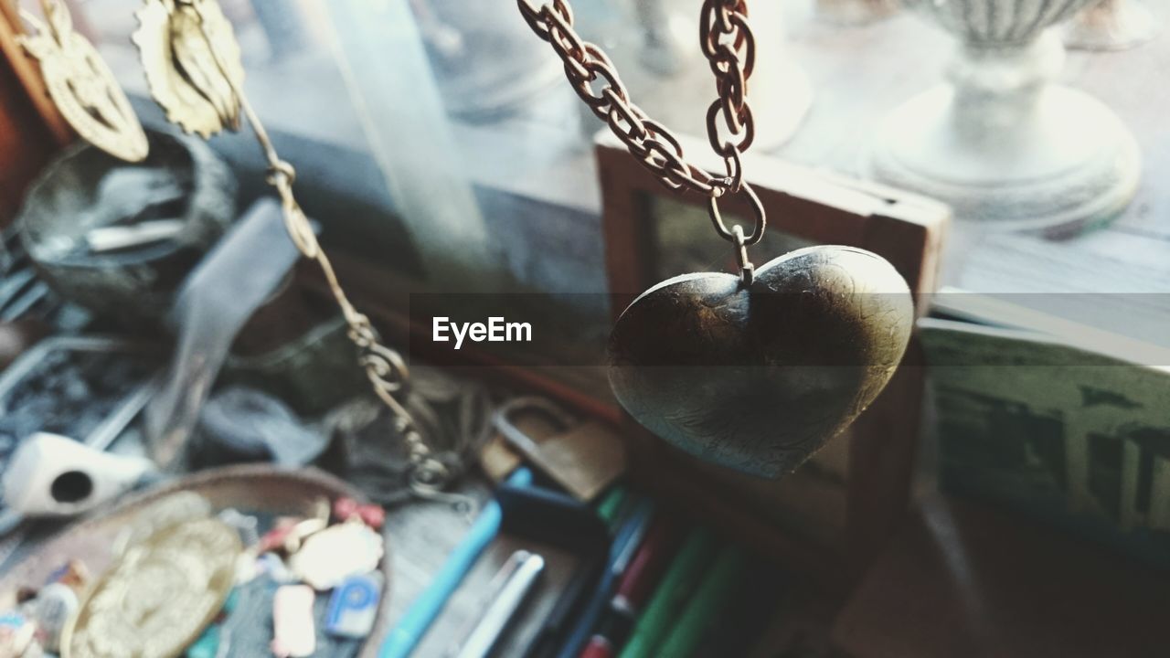 Close-up of heart shape chain against blurred objects on table