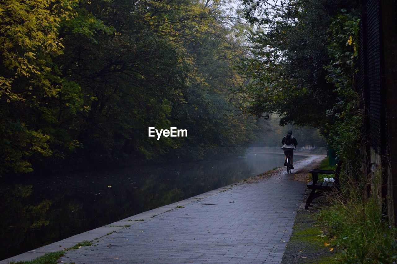 Rear view of person riding bicycle on sidewalk of river